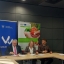 3 osoby siedzace przy stole podpisuja dokumenty, obok stojaca kobbieta